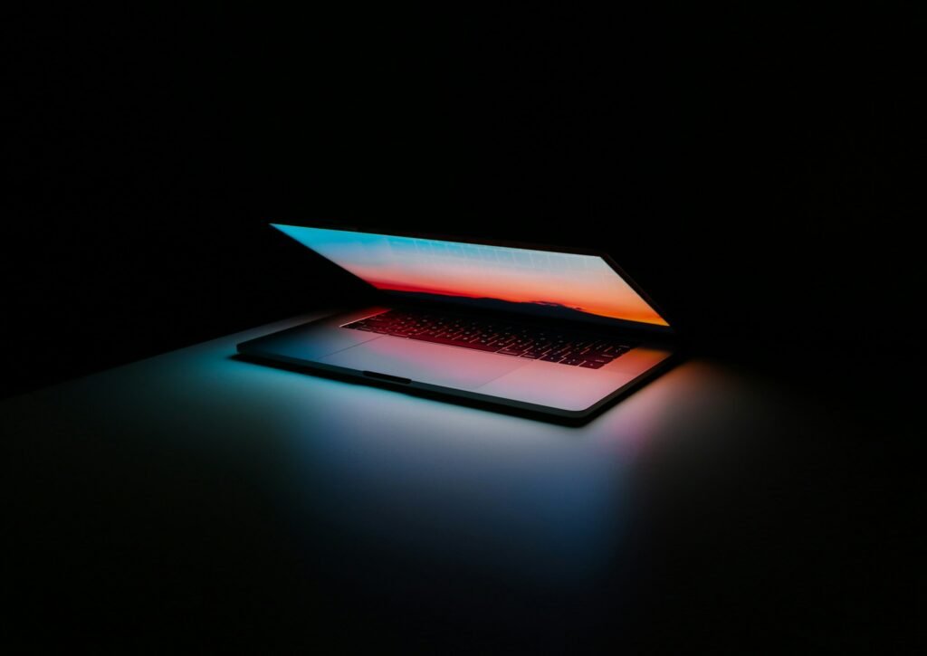 Black background with a laptop screen half open projecting light from the screen