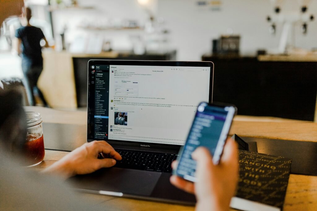 Picture from over the shoulder showing a laptop in the background and a phone in the foreground