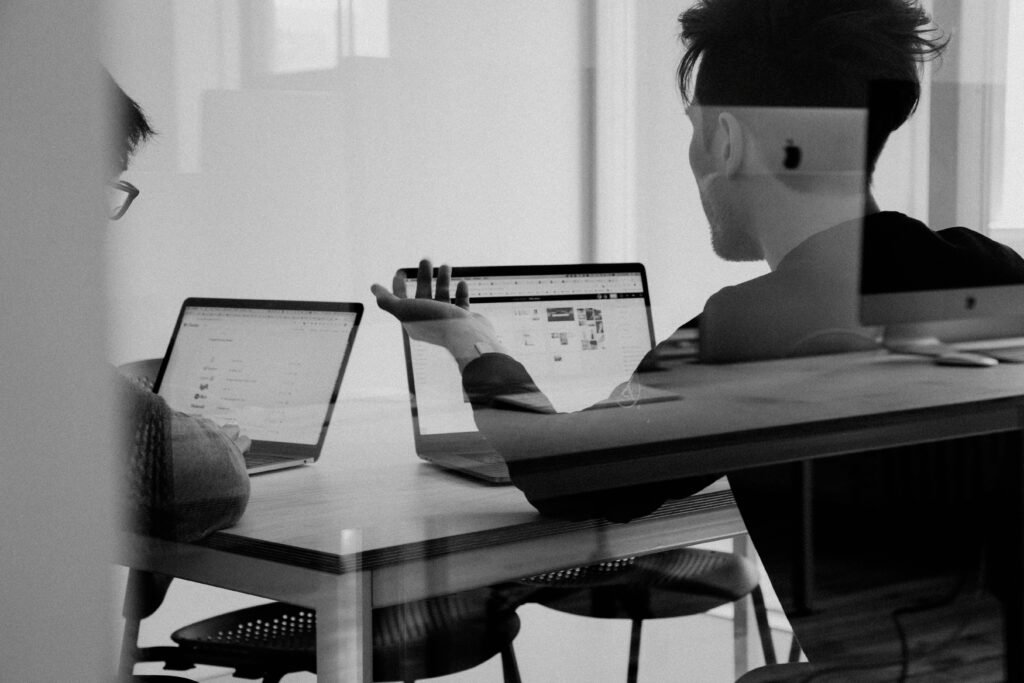 Two people working in an office on laptops in black and white